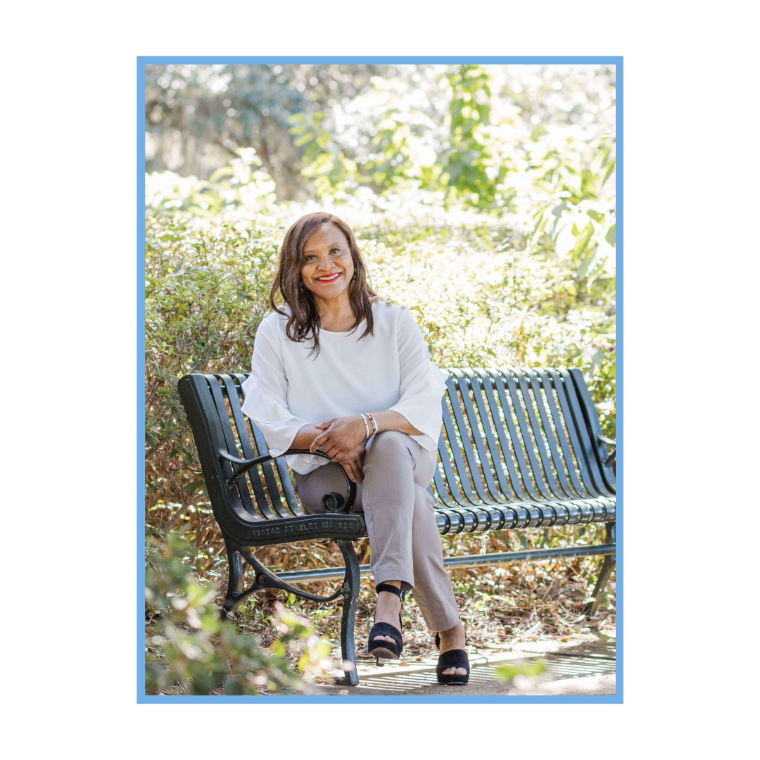 Sharon Redman smiling and sitting on a bench, left leg crossed over the right leg