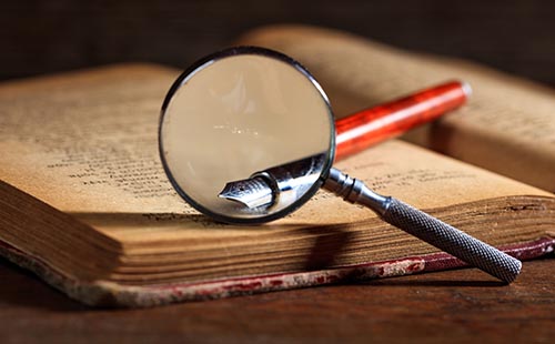 Ink pen and magnifying glass on old book.
