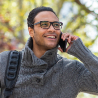Man on his phone with glasses on smiling with a woodland background