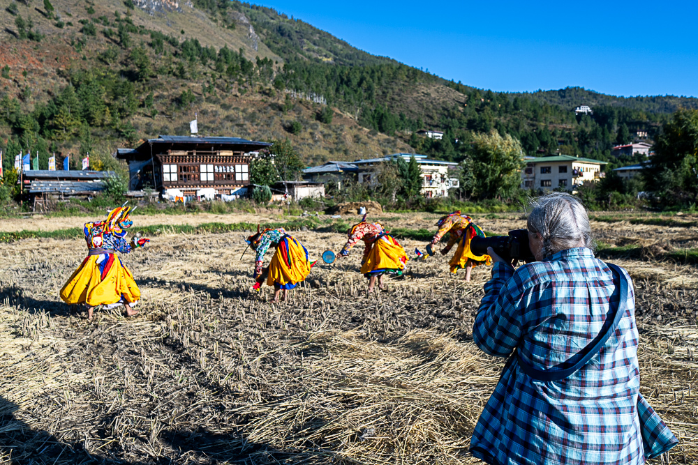 Group of traditional masked dancers performing in Bhutan courtyard - Raw Tours cultural photography.