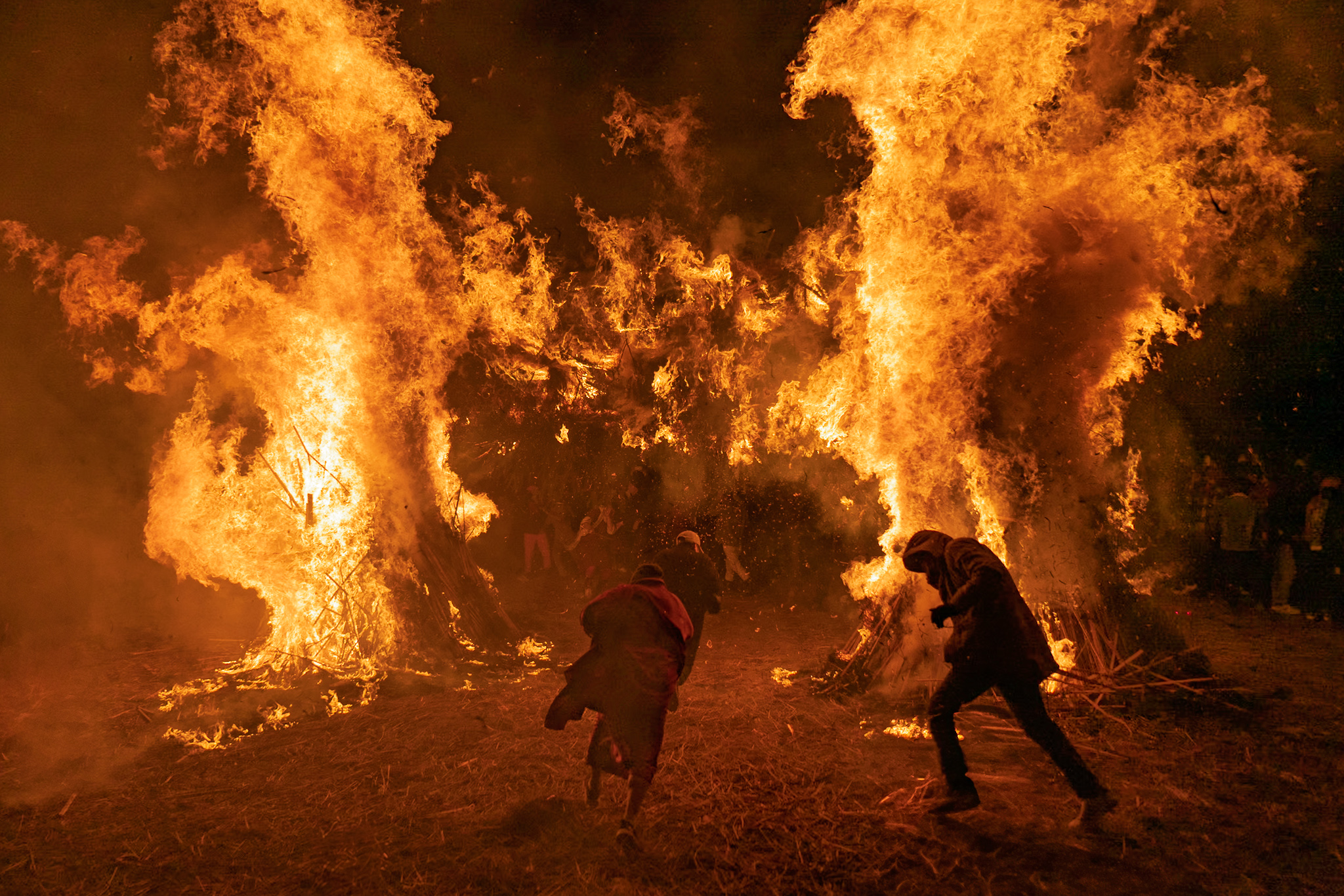 Intense flames illuminate participants during Bhutanese fire ceremony at night.