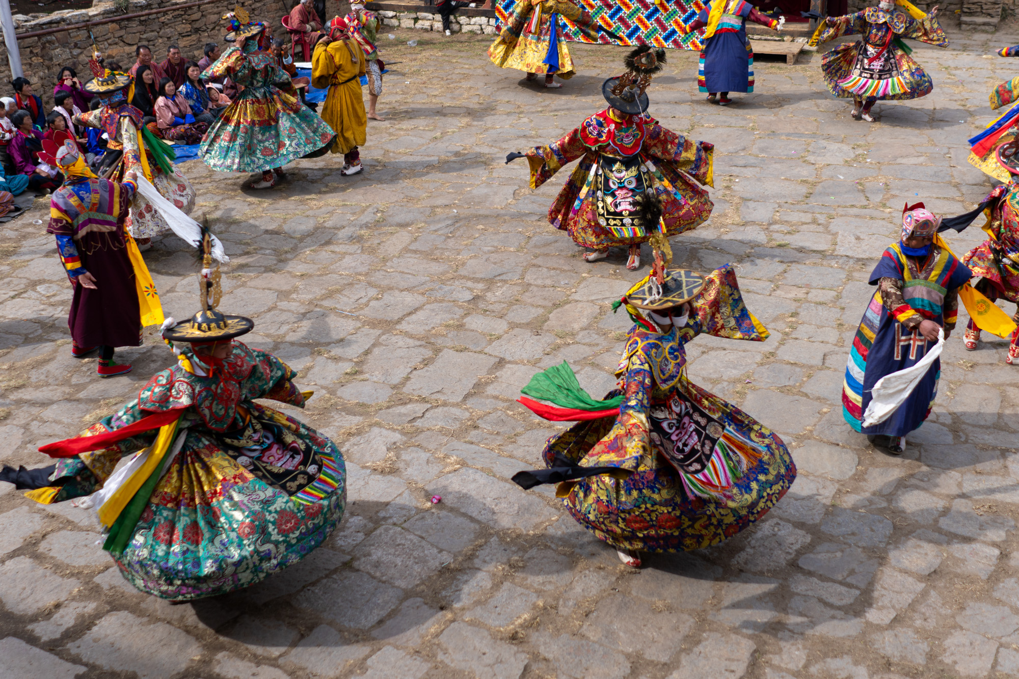 Colorful dancers performing in a circle at Bhutanese outdoor festival - photographed with Raw Tours.