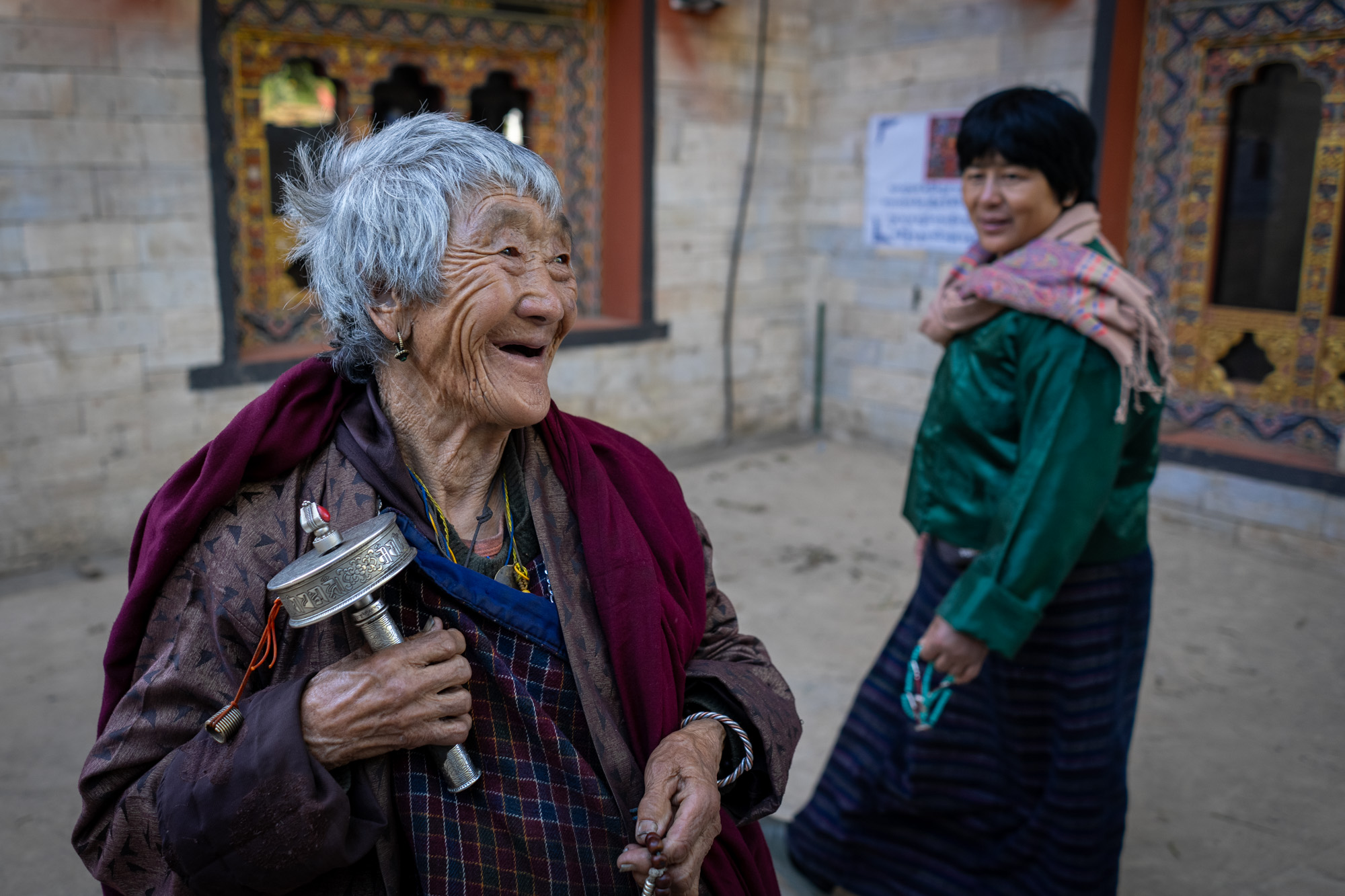 Elderly Bhutanese woman with prayer wheel smiling - cultural portrait from Raw Tours Bhutan photo tour