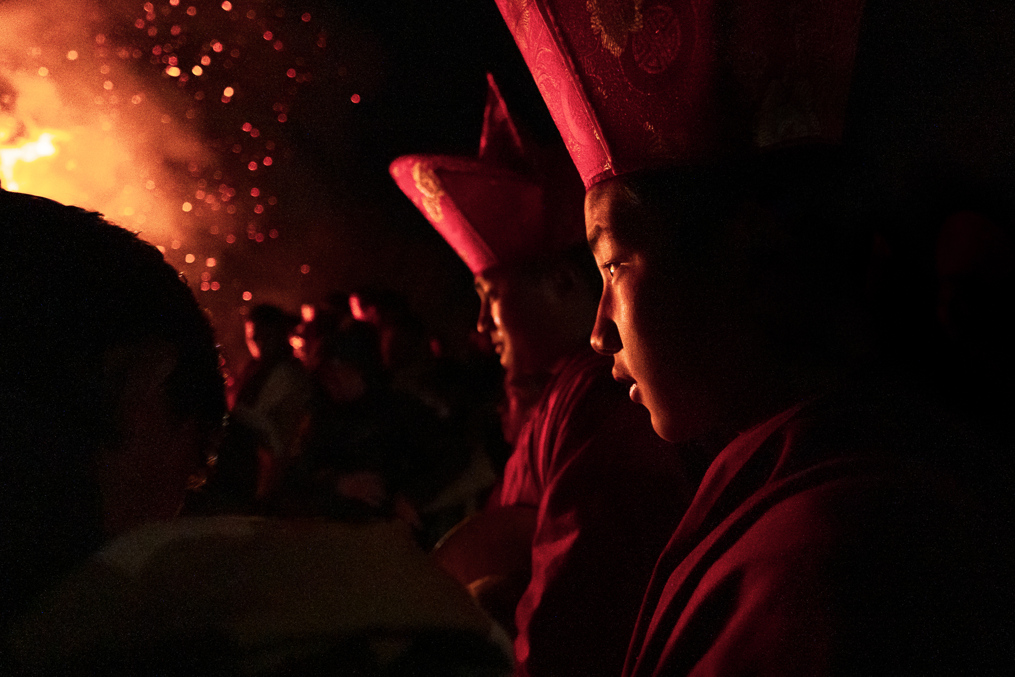 Bhutanese figures in traditional hats observing a glowing night fire ceremony - Raw Tours cultural experience.