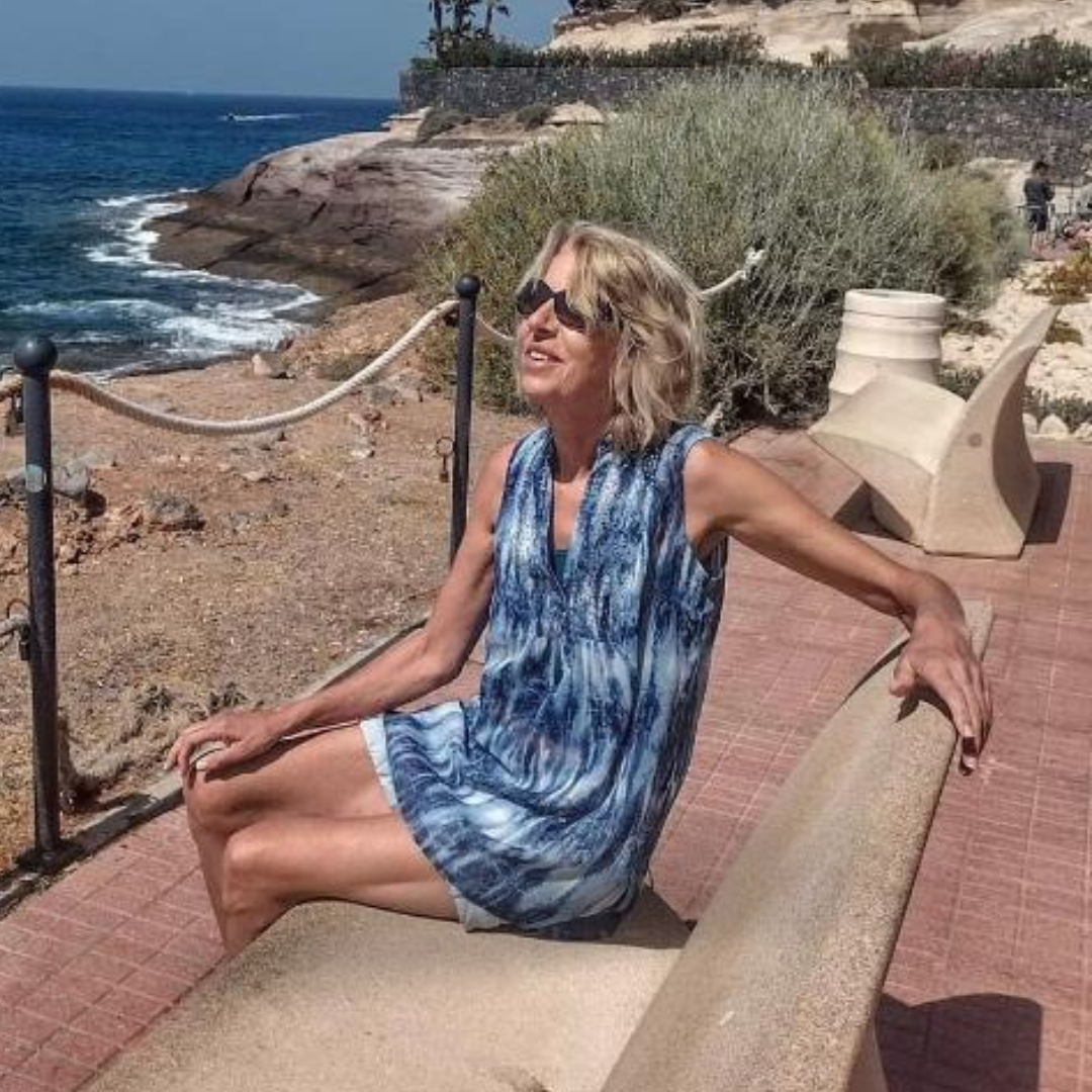 A lady sitting on a bench smiling looking up at the sky