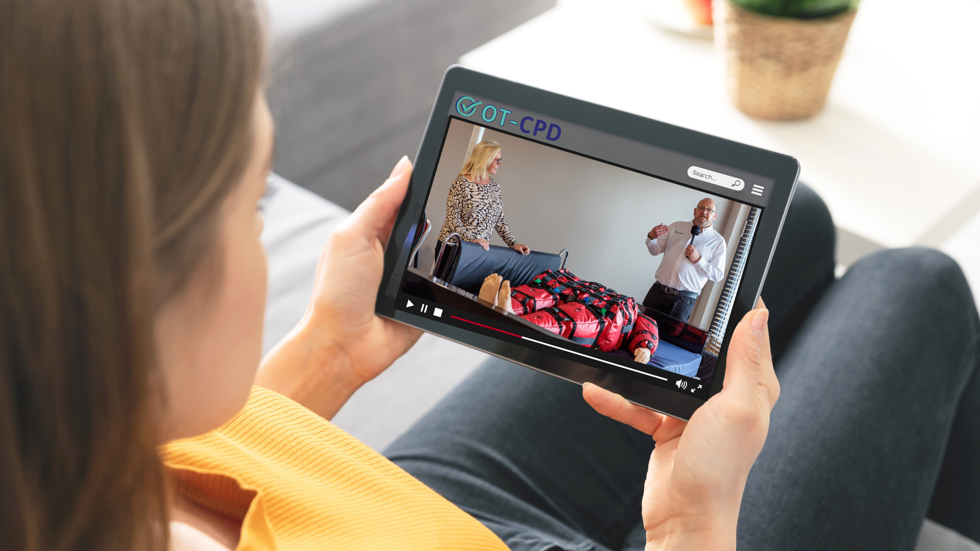 Young man sitting in an office and delivering a webinar. He has his laptop open and is waving at zoom participants.